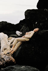 Model wearing a taupe linen blazer and trouser posing on a rock by the beach