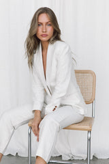 Model wearing white linen suit posing on a chair in a studio