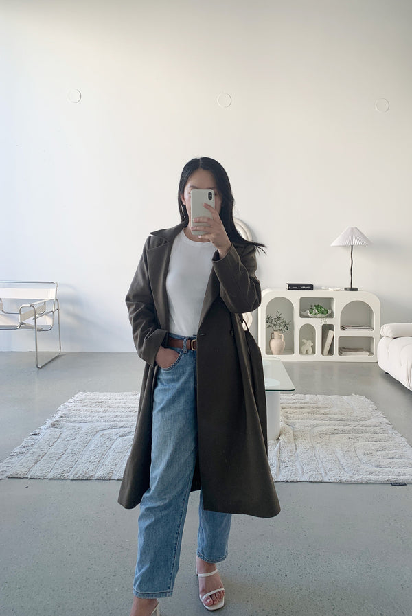 Petite woman wearing brown wool cashmere coat, white tank top and jeans taking selfie in a mirror