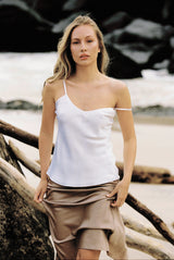 Woman wearing white silk camisole and taupe silk slip skirt by the beach