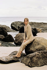 Model wearing a taupe linen blazer and trouser posing on a rock by the beach