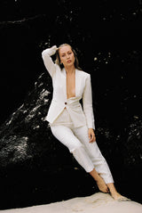 Model wearing white linen suit posing on a rock by the beach