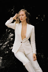 Model wearing a white linen blazer and trouser posing on a rock by the beach