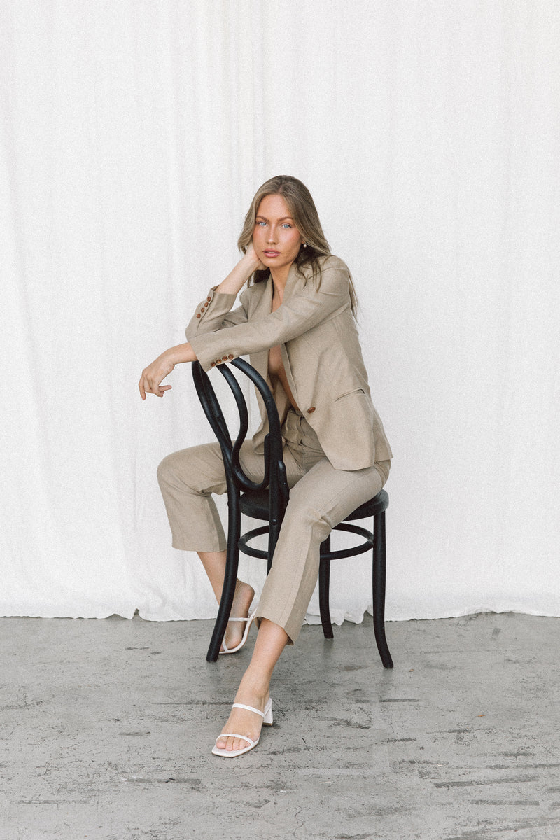 Model wearing a taupe linen blazer and trouser posing on a chair in a studio
